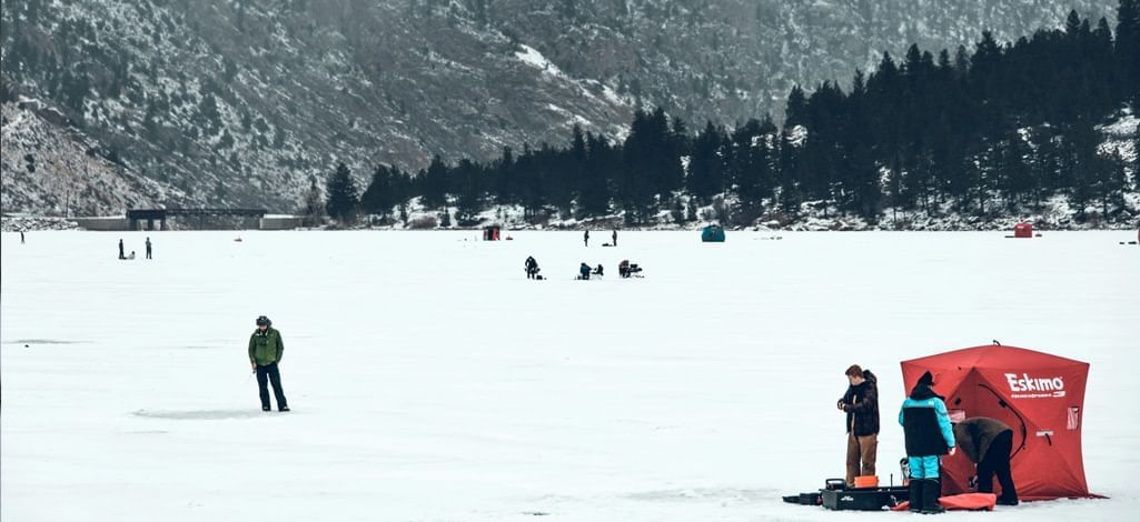 Ice fishing on a frozen lake with red tents and scattered fishers.