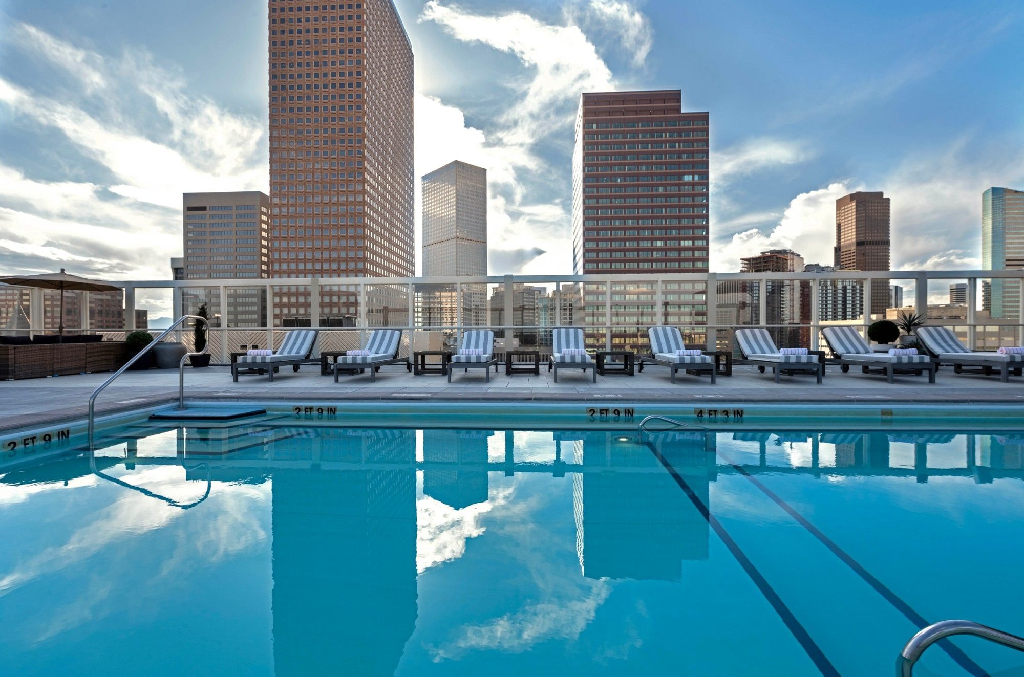 Rooftop Pool by striped chairs under a bright sky near towering city buildings at Warwick Denver