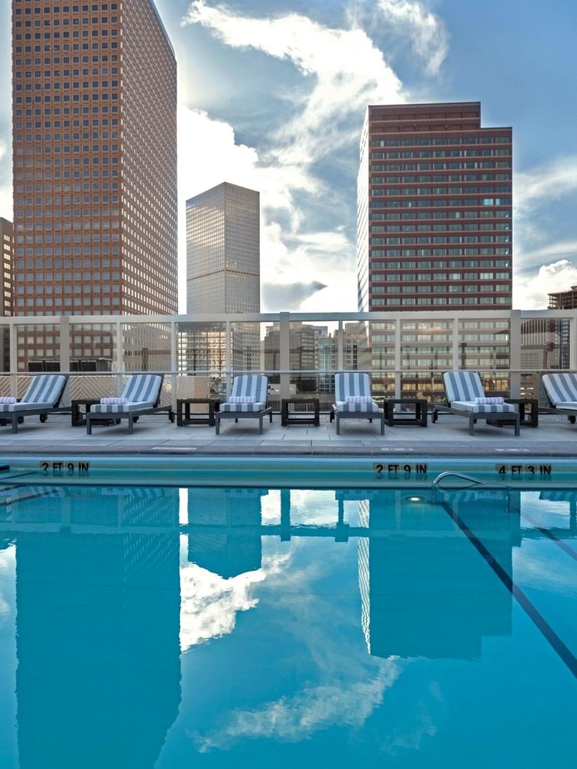 Rooftop Pool by striped chairs under a bright sky near towering city buildings at Warwick Denver