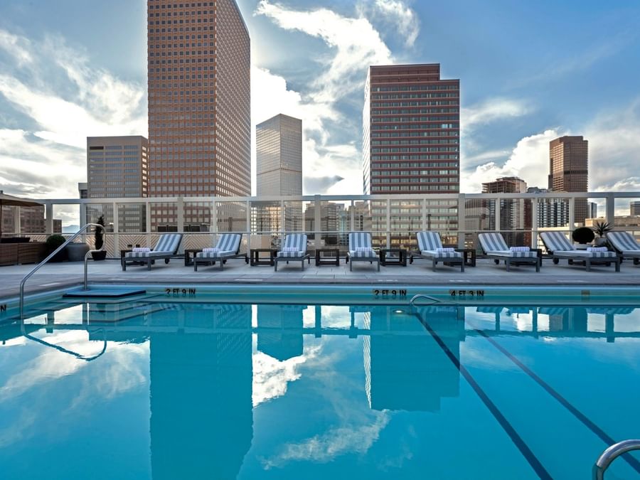 Rooftop Pool by striped chairs under a bright sky near towering city buildings at Warwick Denver