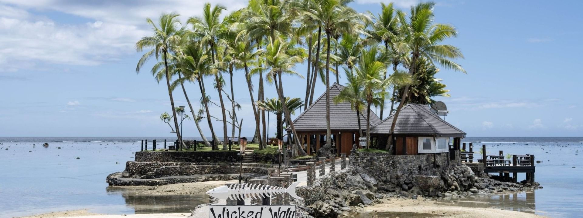 Exterior view of Wicked Walu with a stone path under tall palm trees at Warwick Fiji Resort and Spa