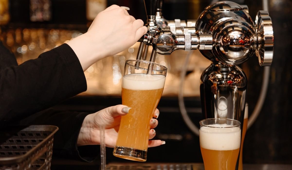 Barman sirviendo un vaso de cerveza de barril desde un grifo cromado en Camino Real Hotels