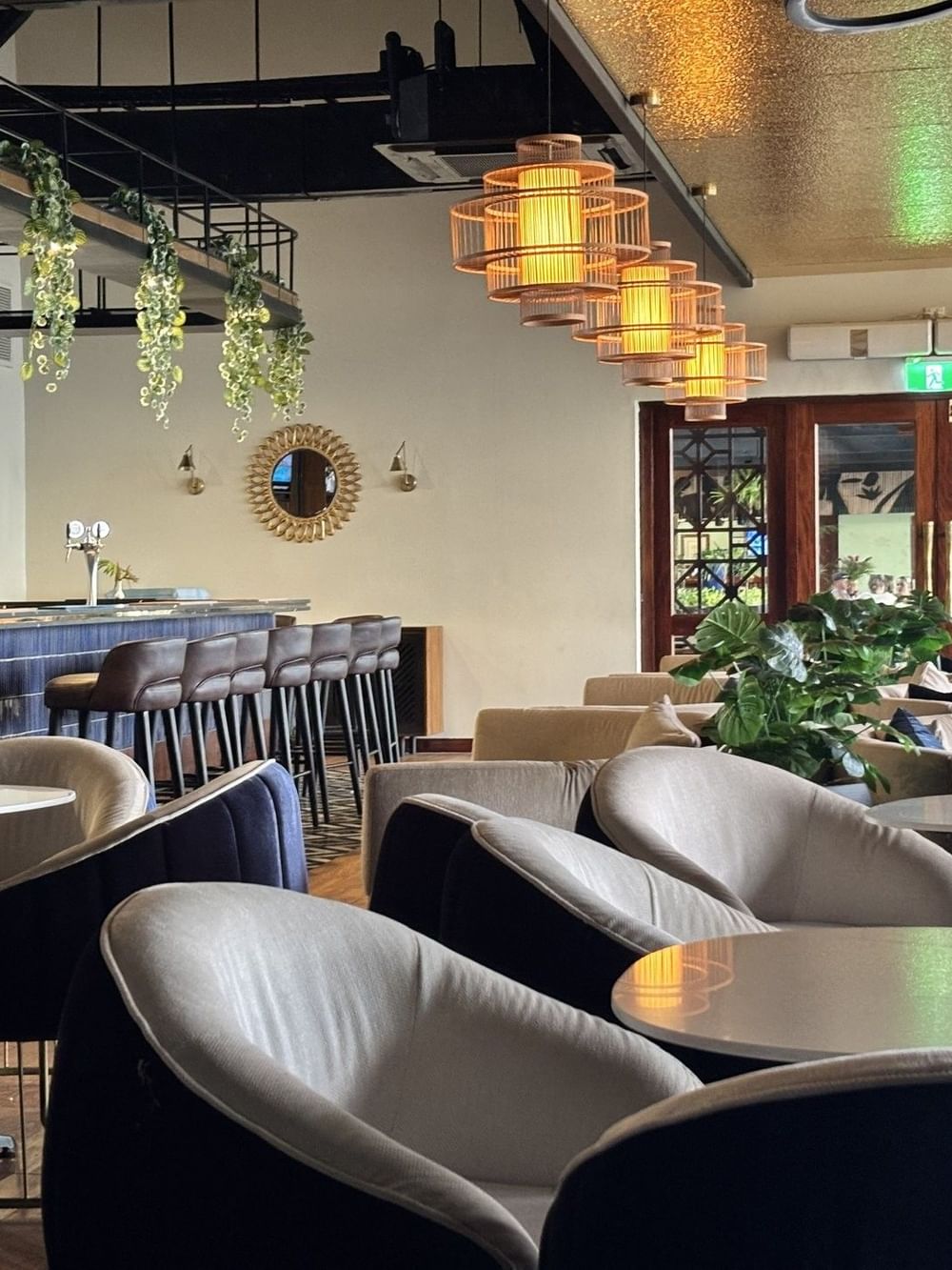 Hibiscus Lounge with brown stools by round tables under hanging plants and cage lamps at Warwick Fiji Resort and Spa