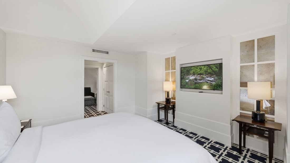 Deluxe King Suite with white bedding, wall-mounted TV, and geometric patterned carpet at el PRADO Hotel Palo Alto.
