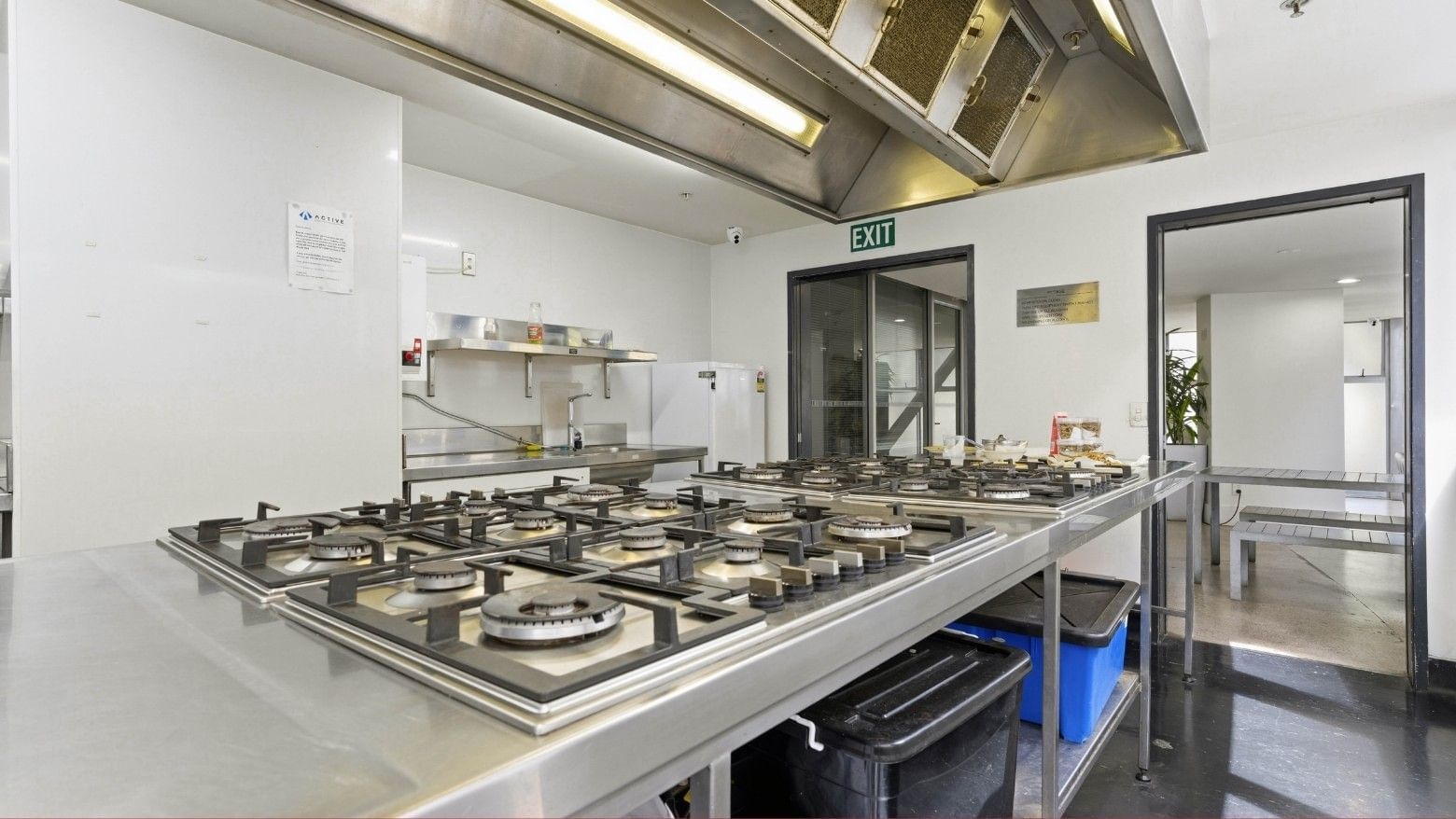Stainless steel kitchen with multiple gas stoves and an exit sign above the door.