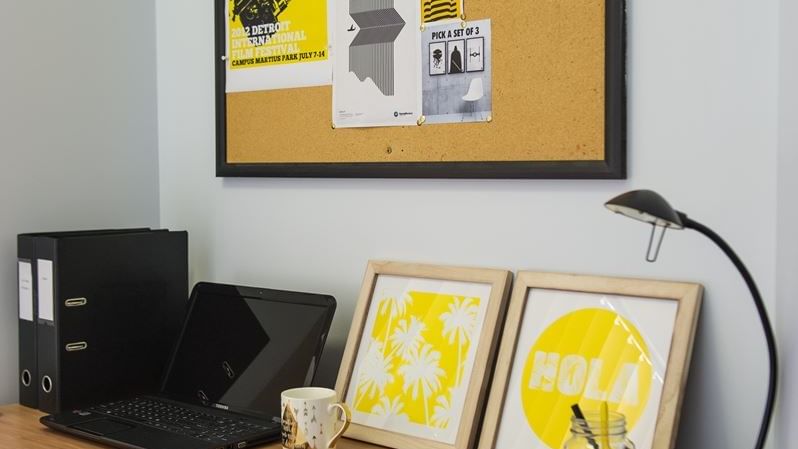 Wooden desk with laptop, desk lamp, framed artwork, and cork board with posters at StudentLiving - on Margaret