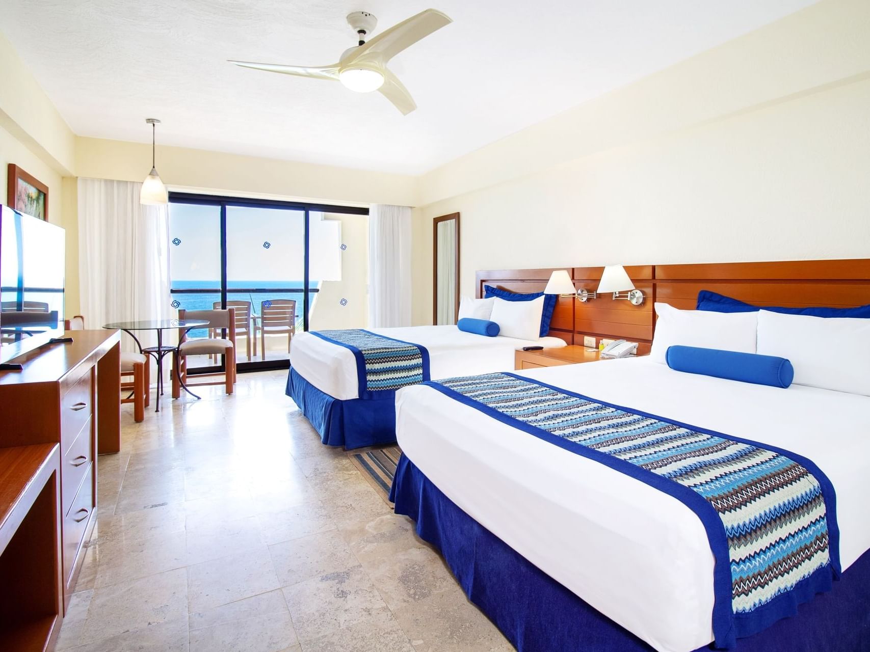 Suite with two beds & blue bedding, by a balcony with chairs, and an ocean view at Guadalajara Plaza Hoteles & Suites