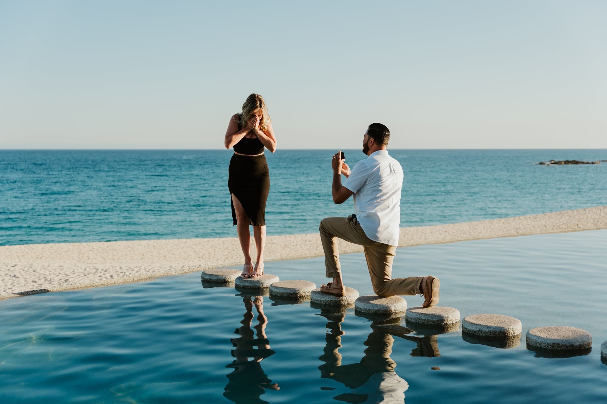 Man kneeling on stones over the pool, proposing to a woman at Marquis Los Cabos