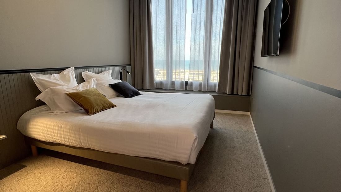 Chambre d'hôtel avec lit king size, télévision murale, et vue sur la mer par la fenêtre.