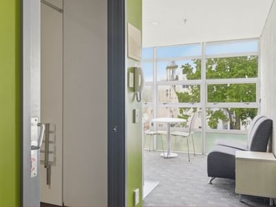 A lounge area with a couch and a table by a large window at Student Living Auckland - Beach.