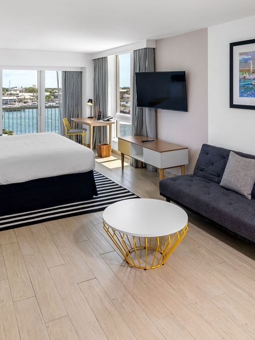 Harbour Premium Balcony with a bed by a striped rug and a dark sofa under colorful art at Warwick Paradise Island Bahamas
