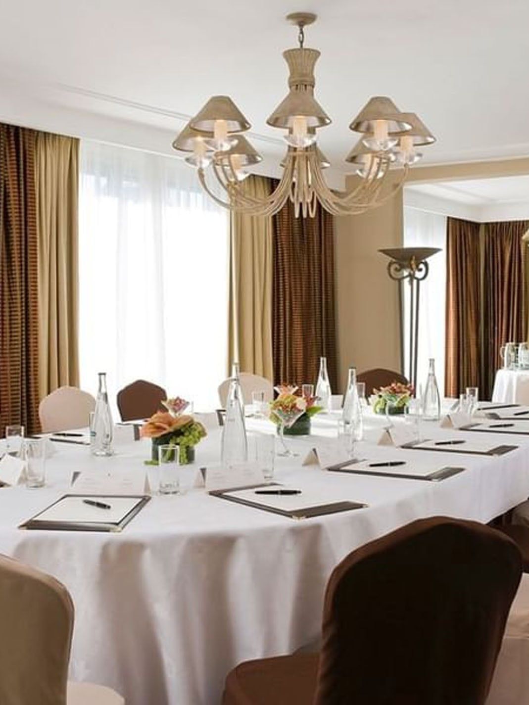 Plush chairs surrounding an oval table under a large beige chandelier in Presidential Suite at Warwick Paris Champs Elysées