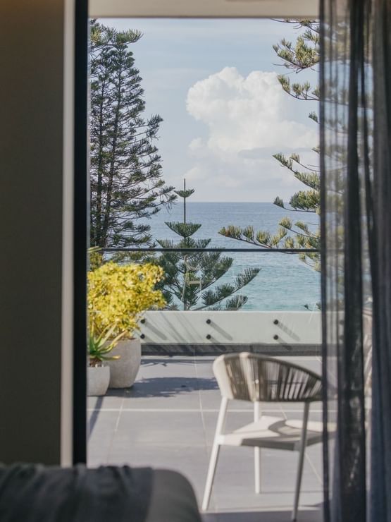 Elysium Suite at Elysium Manly, showing a chair by a terrace door with trees and the sea, an elite hotel in Manly