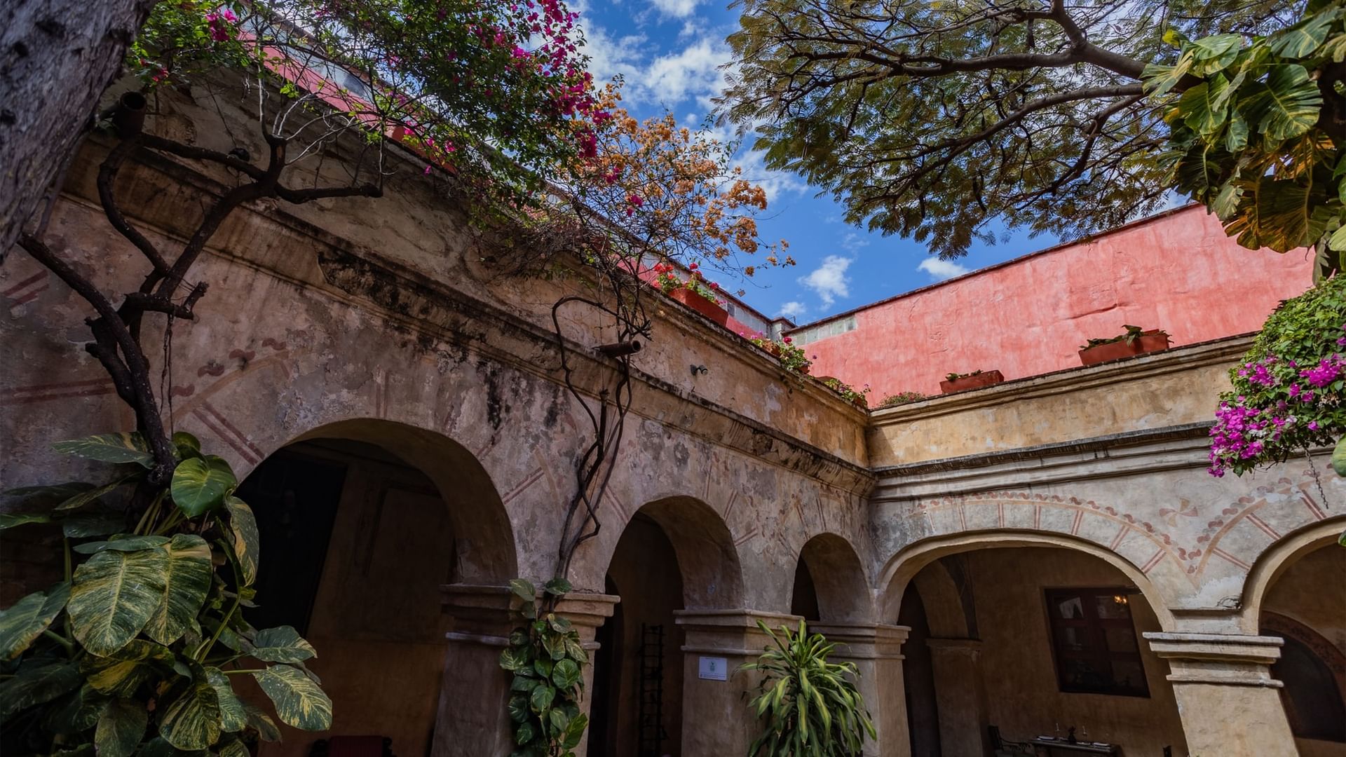 Historic courtyard with stone arches and vibrant pink flowers under blue skyat Quinta Real Oaxaca