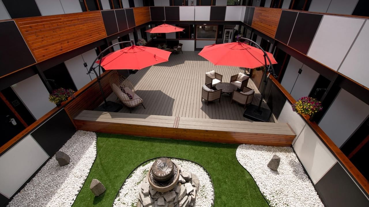 An outdoor lounge with red umbrellas, wooden deck and green turf surrounding a central stone feature.