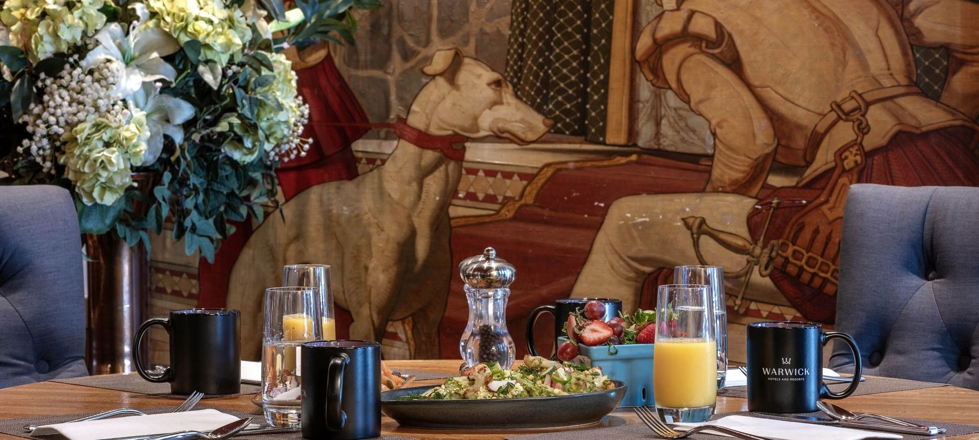 Breakfast table with orange juice and black mugs set against a vintage dog mural in Murals on 54 at Warwick New York