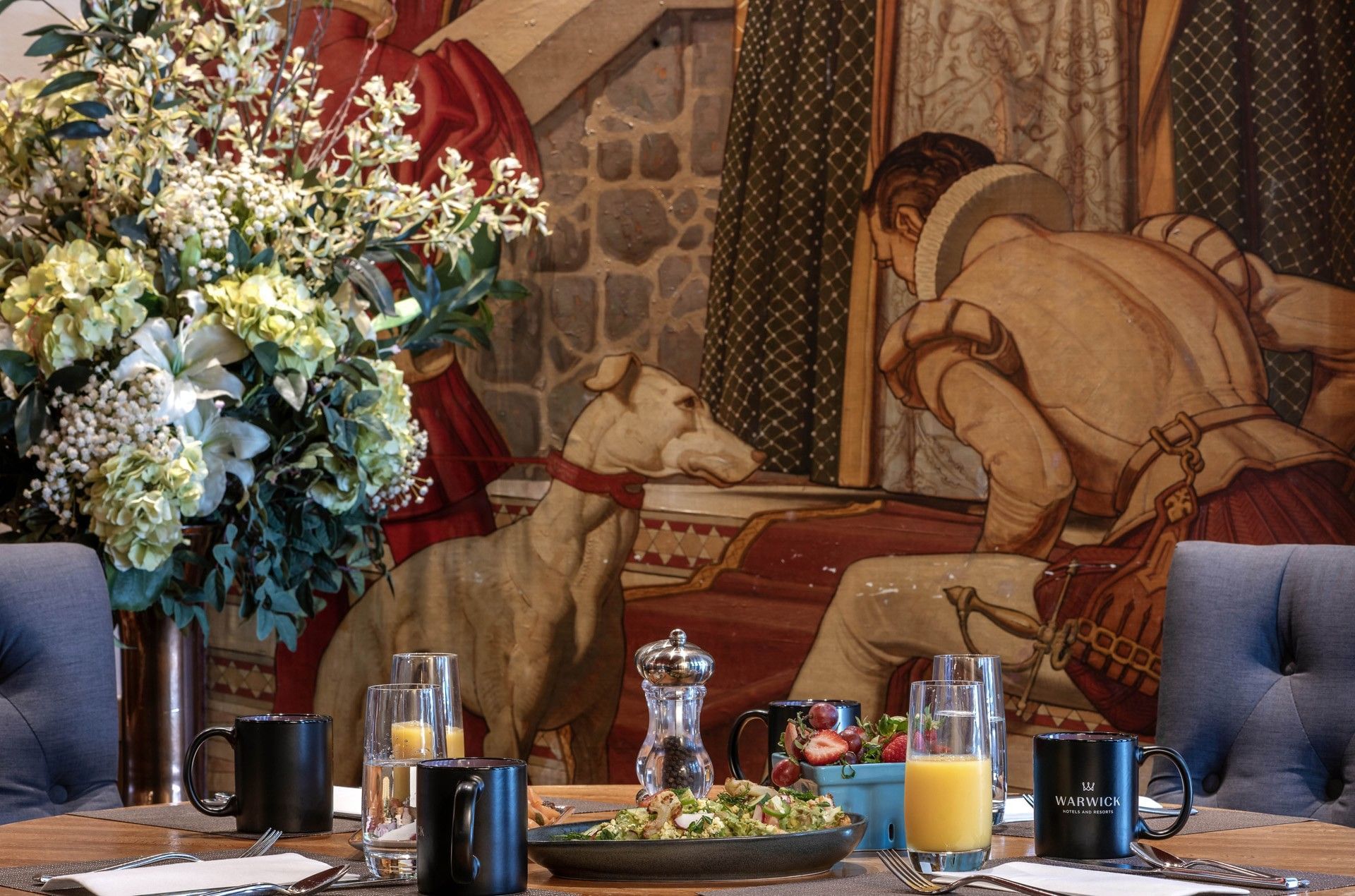 Breakfast table with orange juice and black mugs set against a vintage dog mural in Murals on 54 at Warwick New York