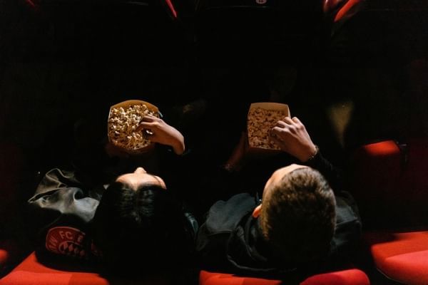 An aerial shot of a man and woman in a dim movie theatre with their hands in popcorn buckets.