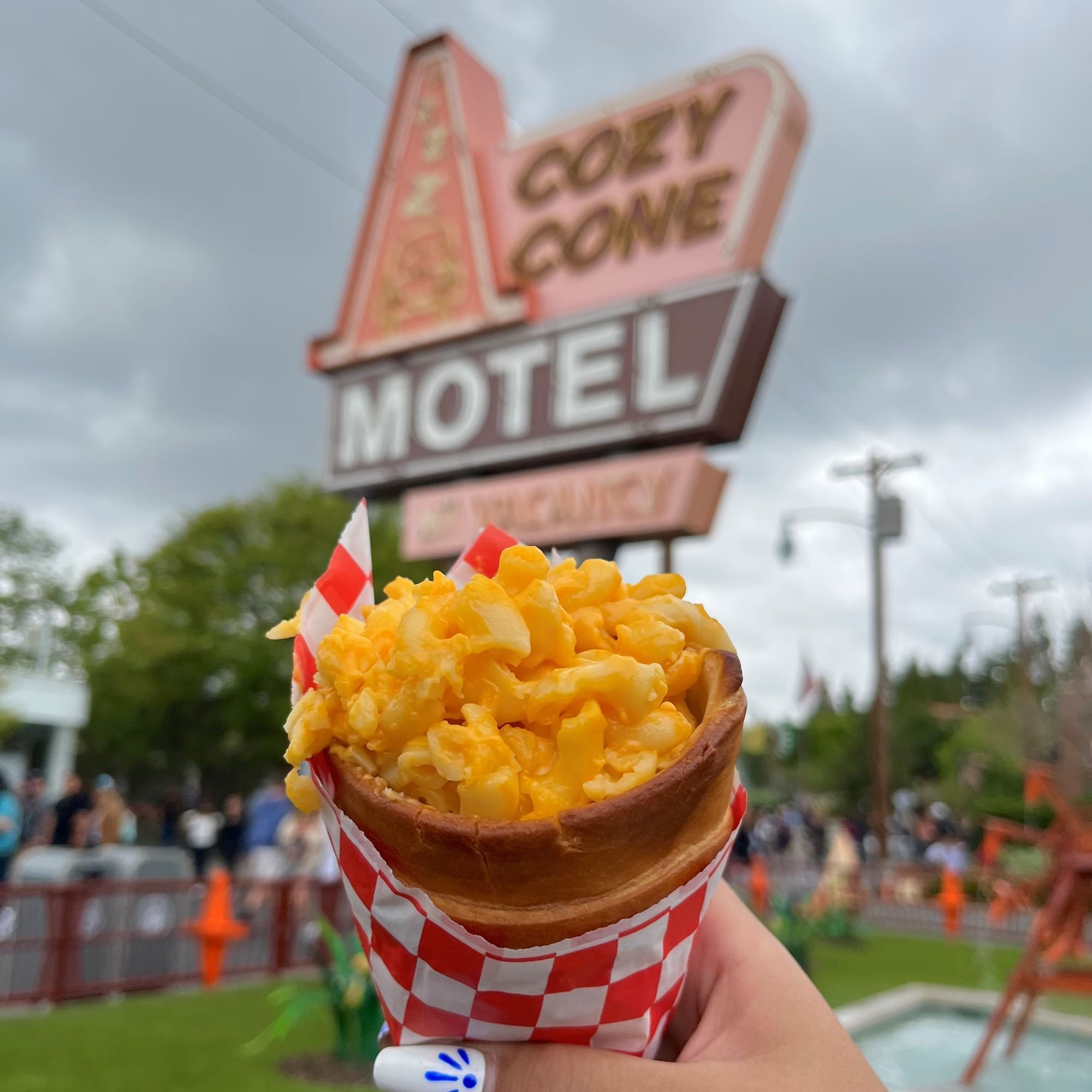 a hand holding a cone of macaroni and cheese in front of a motel sign