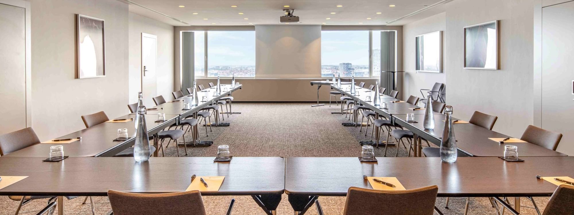 Meet 26 One Meeting room with long tables, chairs, and city view through windows at The Hotel Brussels
