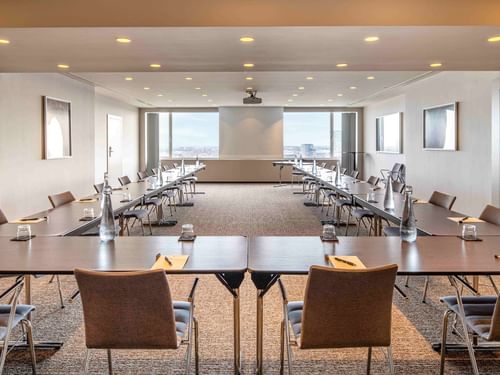 Meet 26 One Meeting room with long tables, chairs, and city view through windows at The Hotel Brussels