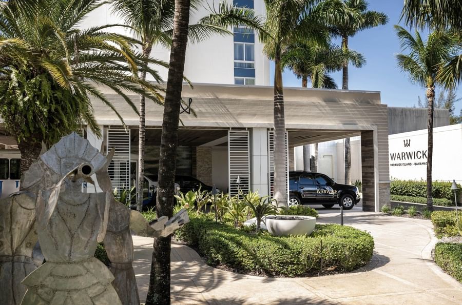 Metal sculpture by palm trees and a black vehicle under a modern porte-cochère at Warwick Paradise Island Bahamas