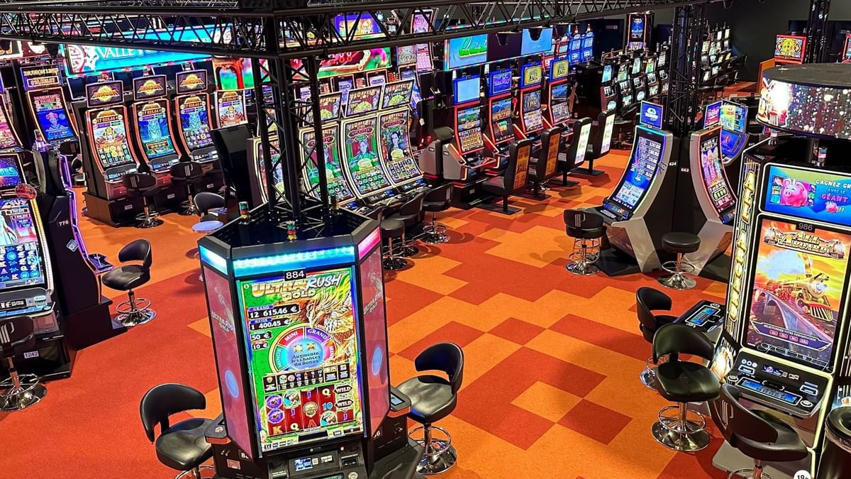 Salle de jeux avec des machines à sous et des chaises, éclairage au plafond et message de prévention en bas.
