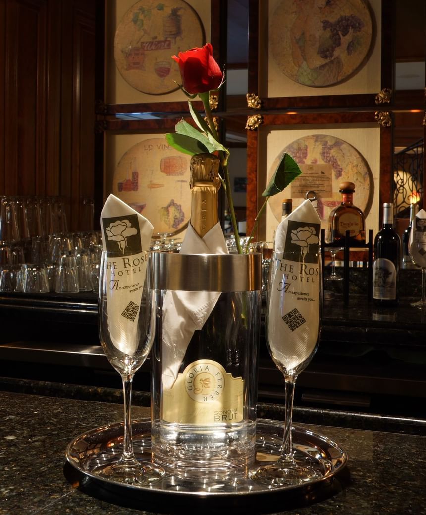 Sparkling wine bottle in an ice bucket and a single red rose on a tray in an elegant bar setting at The Rose Hotel