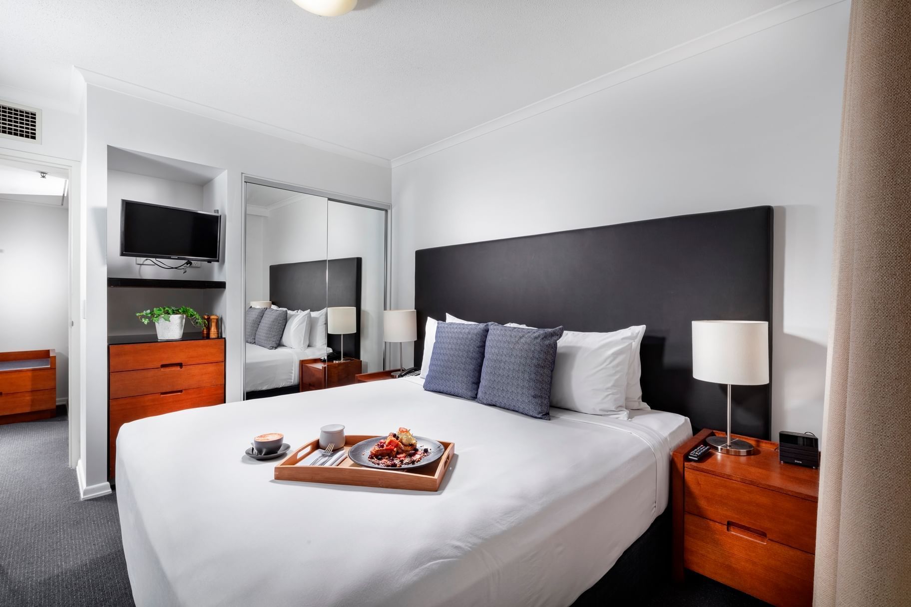 King bed set with a wooden tray of breakfast and modern furnishings in One Bedroom Apartment at The Sebel Brisbane