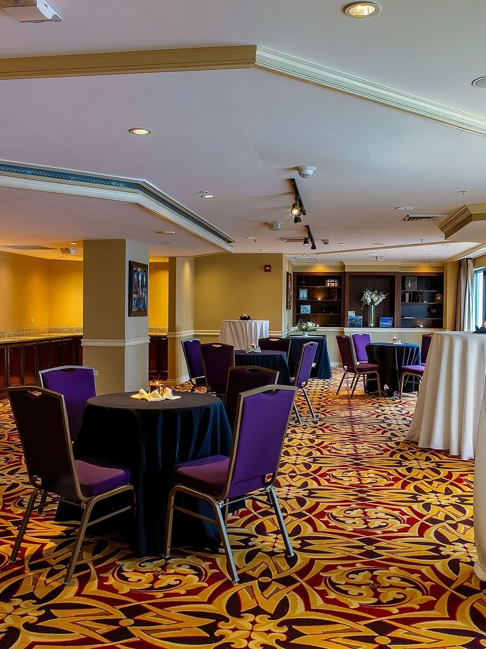 Small round tables with purple chairs surrounding a tall cocktail table in Executive Lounge at Warwick Denver