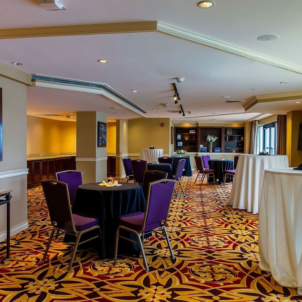 Small round tables with purple chairs surrounding a tall cocktail table in Executive Lounge at Warwick Denver
