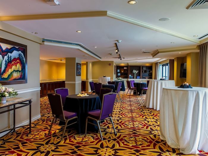 Small round tables with purple chairs surrounding a tall cocktail table in Executive Lounge at Warwick Denver