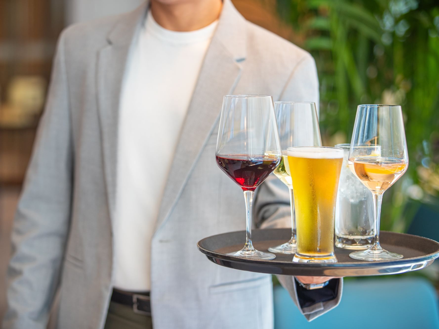 Man in a suit holding a tray with three wine glasses and a pint glass.