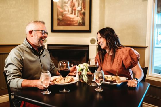 Man and woman smiling and talking over a dinner table in front of a fireplace.