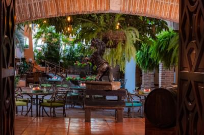 Open doorway reveals outdoor patio with tables, chairs, plants, and a horse statue on a wooden stand.