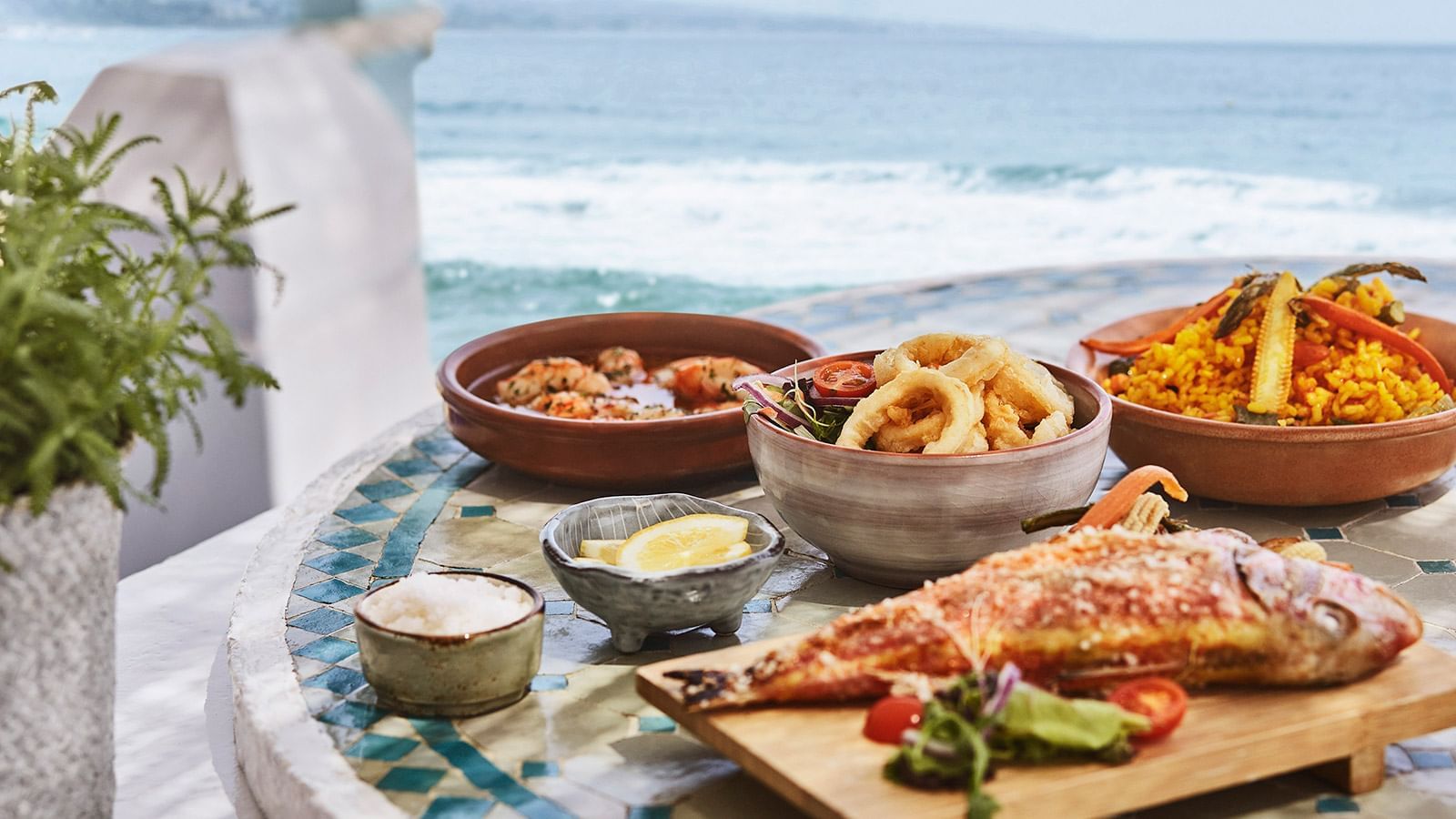 Seafood dishes, including calamari and grilled fish, served on a tiled table near the ocean at Marbella Club
