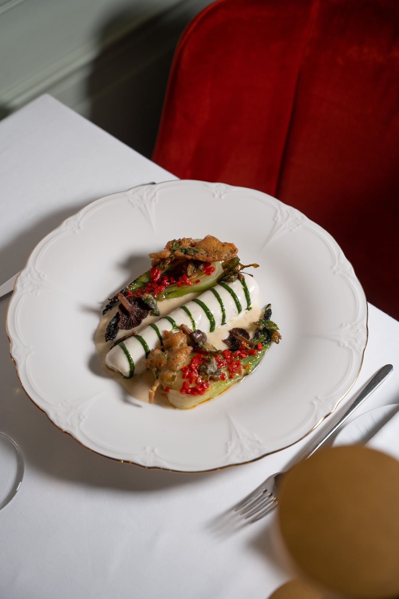Gourmet fish dish with green herb drizzle and vegetables on white china beside red velvet chair at Hotel Westminster Warwick Paris