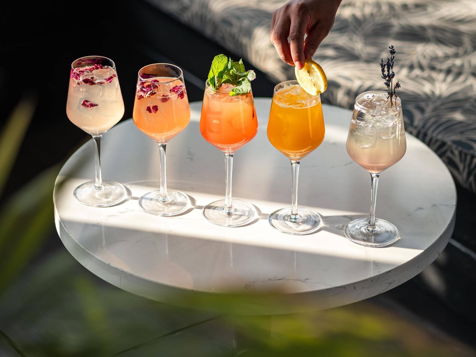 A person placing a lemon slice on a glass, surrounded by five other glasses with drinks.