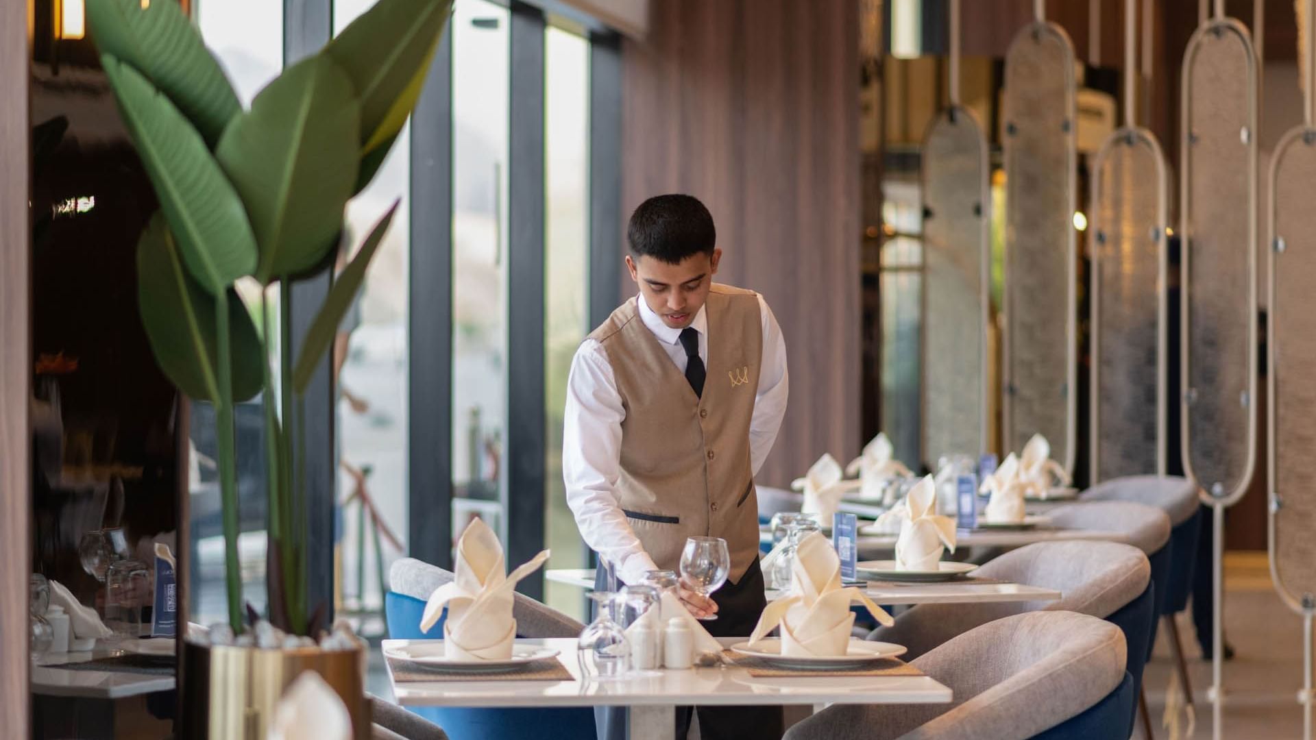 A waiter arranges tables in a restaurant at Warwick Hotels & Resorts