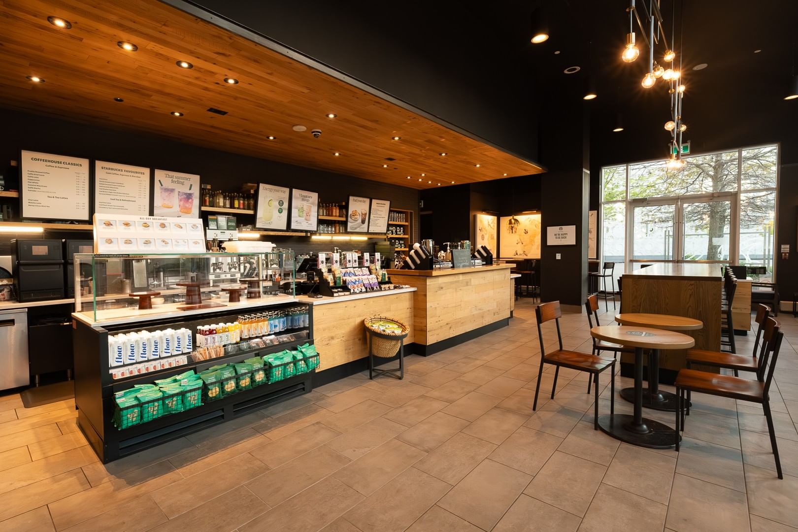 Starbucks cafe with wooden counters and dining tables by large windows under warm ceiling lighting at Hotel X Toronto