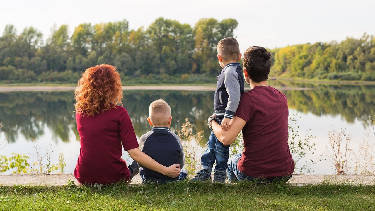 Family of four sitting by the river with green trees in the background.