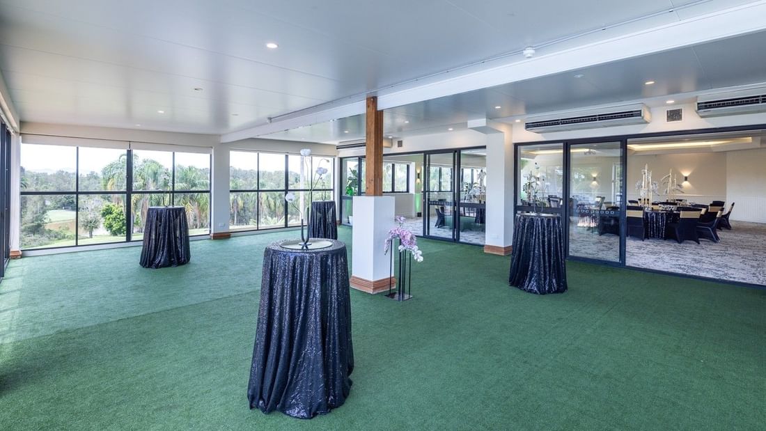 Large room with green carpet, three draped tables, and glass walls showing an outdoor view.