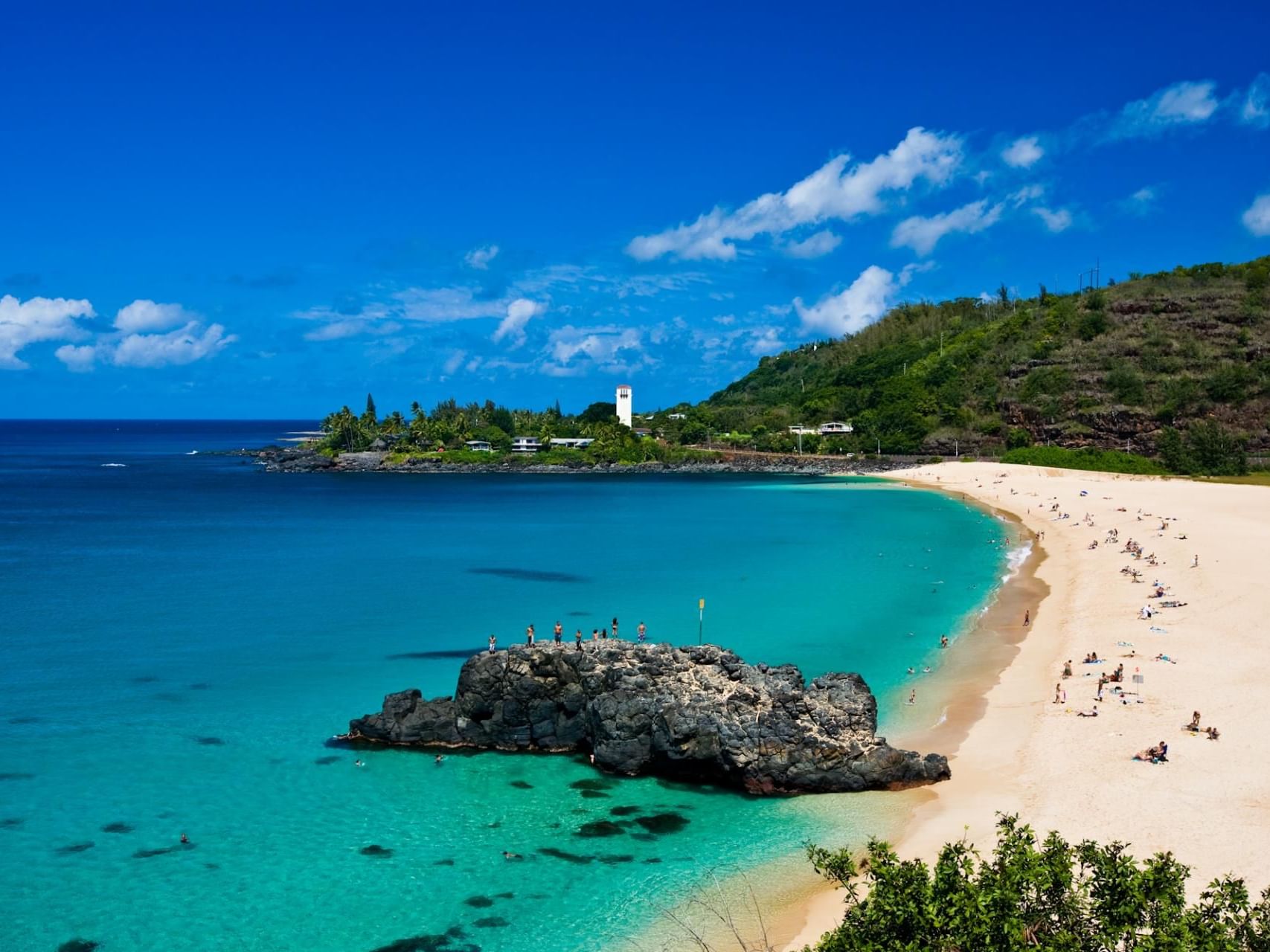 People enjoying the sun and sand in Waimea Bay near Waikiki Resort Hotel