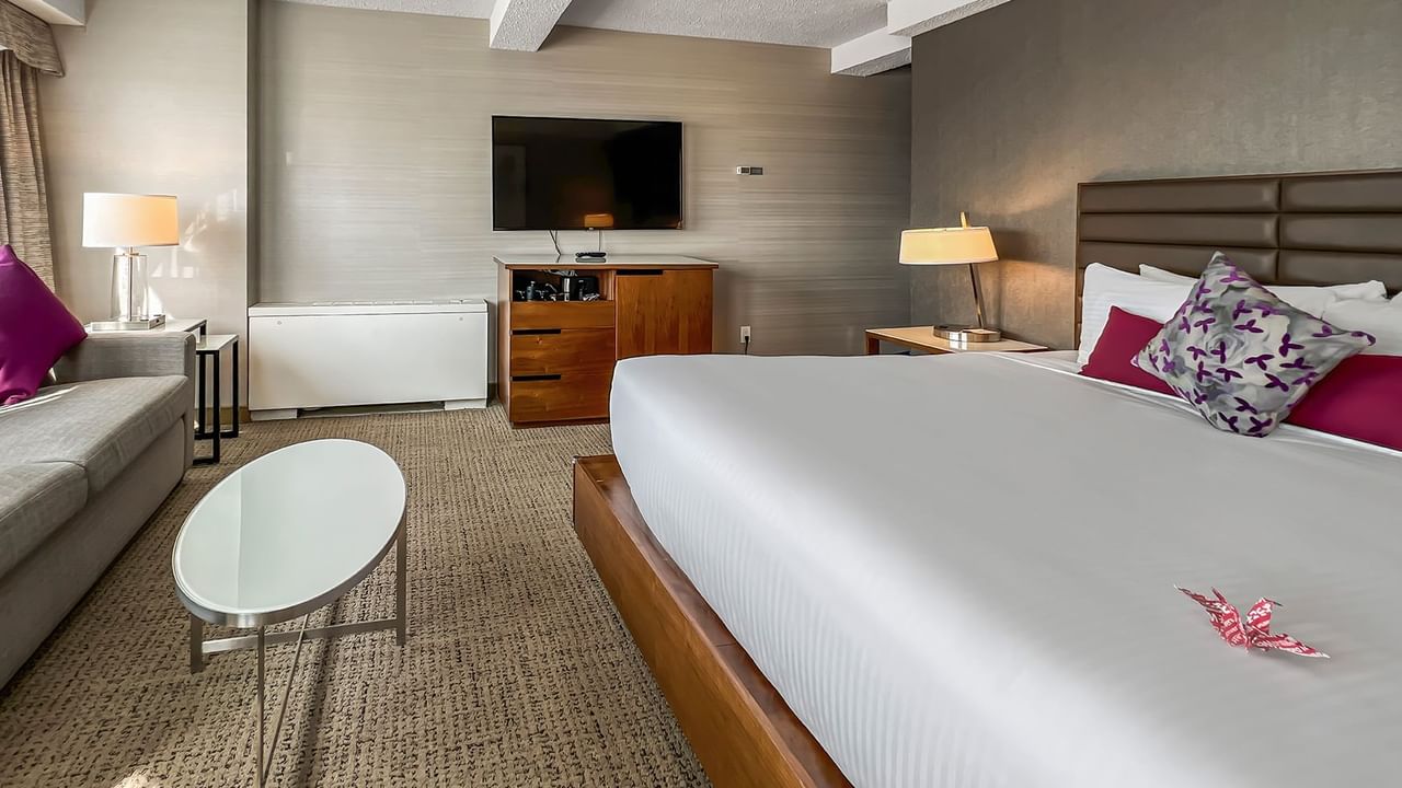 Hotel bedroom with bed, couch, TV, and table