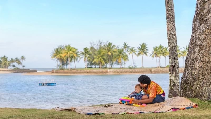 Mother and child playing on a blanket by the beach at The Naviti Resort - Fiji in Korolevu.