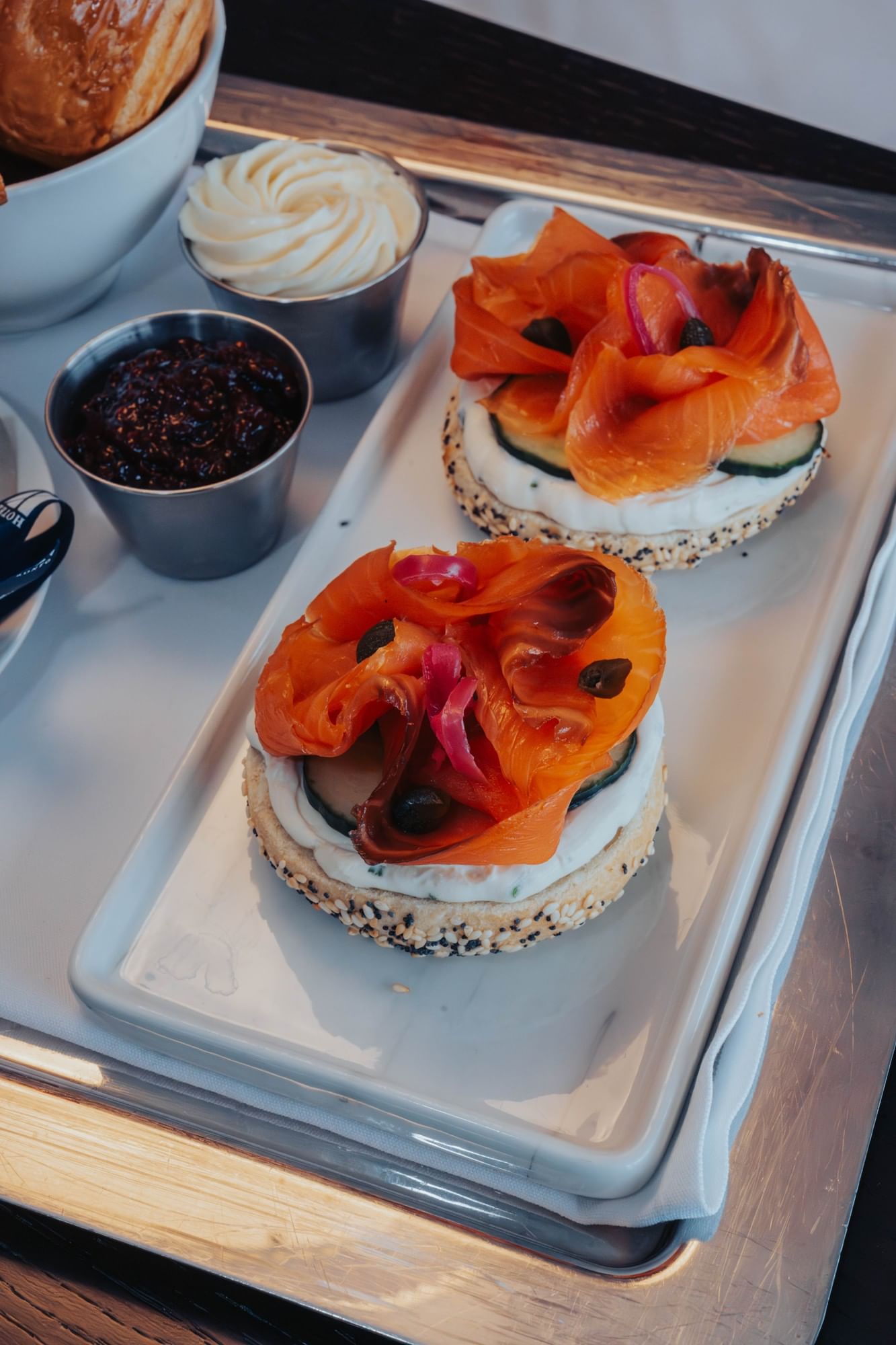 Two smoked salmon bagels topped with capers and pickled onion, beside cream cheese and jam at Hotel X Toronto