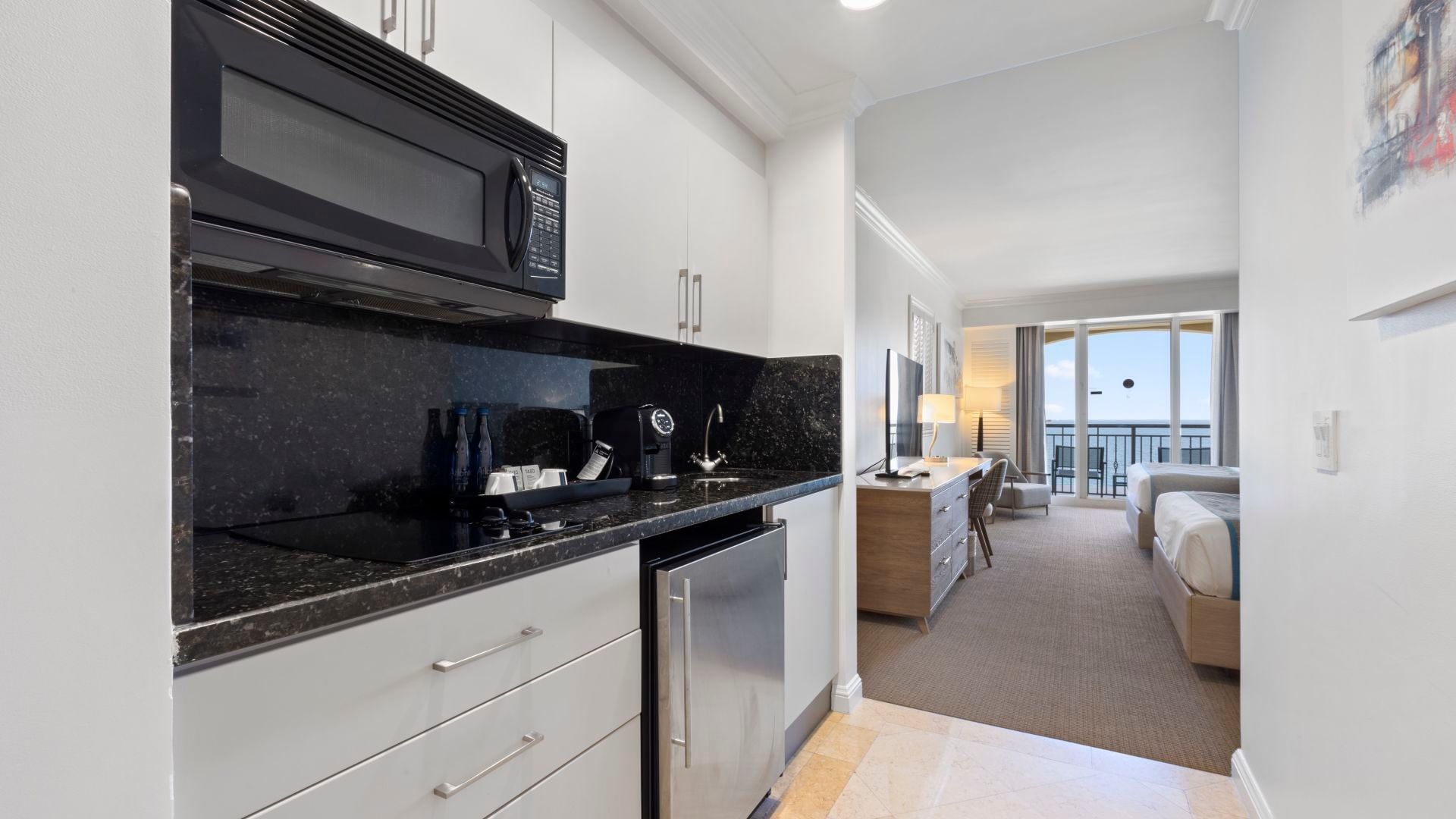 A kitchenette with modern appliances and a living area with a bed in the background.