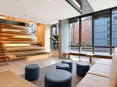 Comfortable lounge area with couches and stools near a staircase at La Trobe University - North and South Apartments.