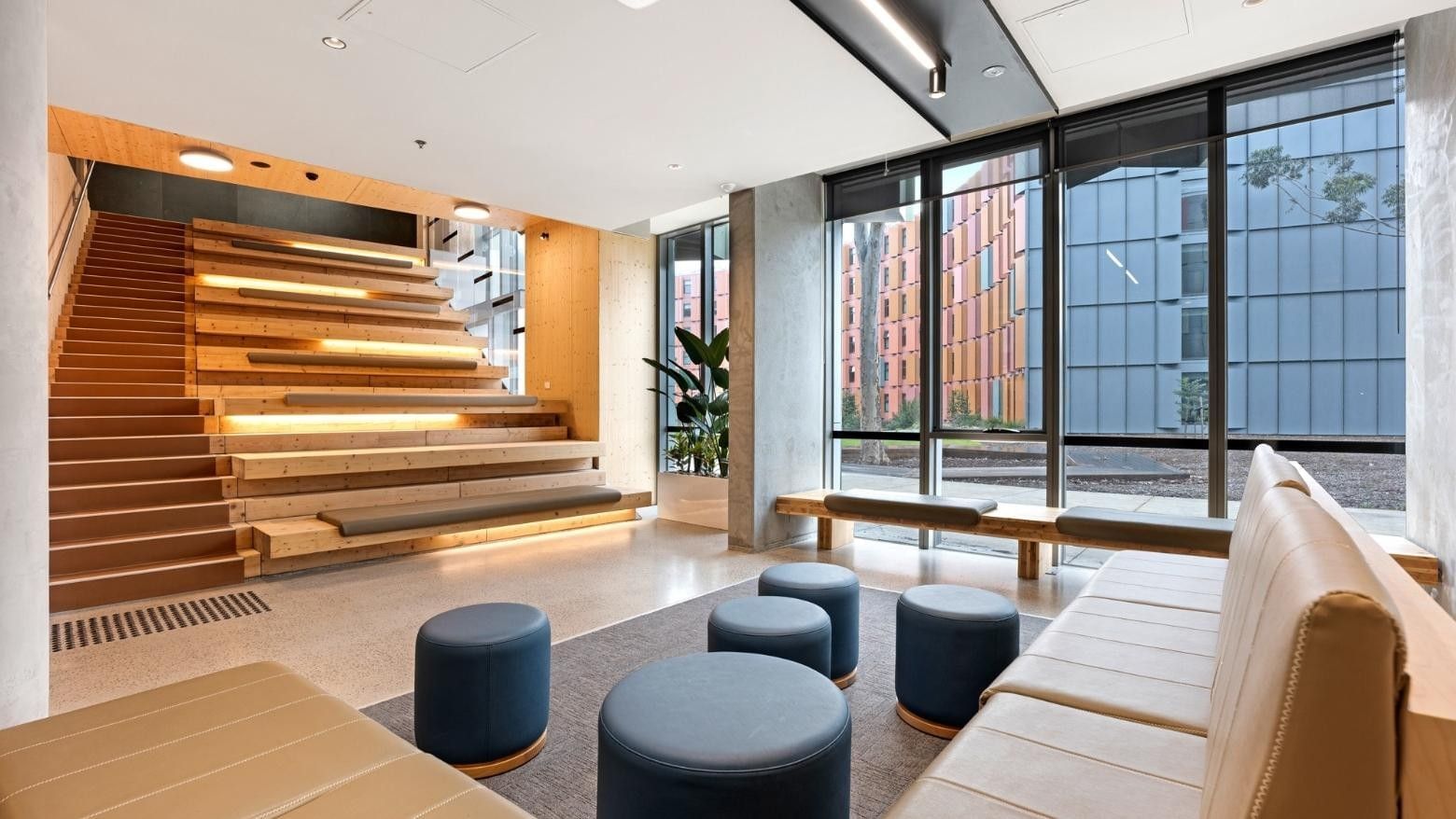 Comfortable lounge area with couches and stools near a staircase at La Trobe University - North and South Apartments.