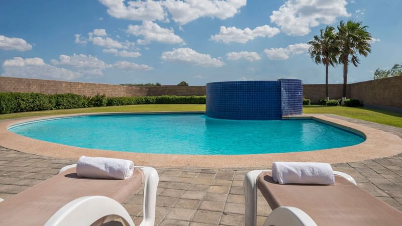 Outdoor swimming pool featuring lounge chairs with towels and a blue fountain at Real Inn Nuevo Laredo